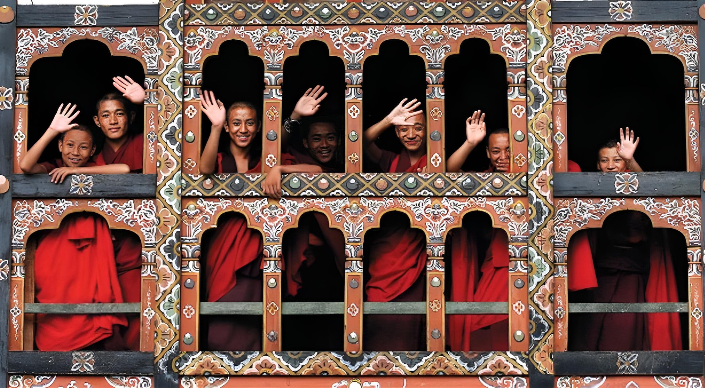 Young monks waving from the painted windows of a dzong