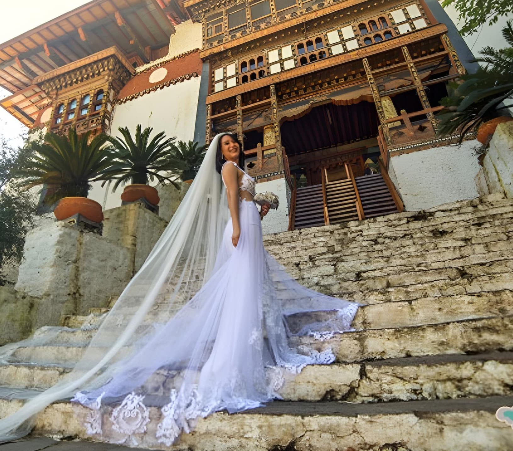 A bride in a white gown on the stone steps of a Bhutanese dzong