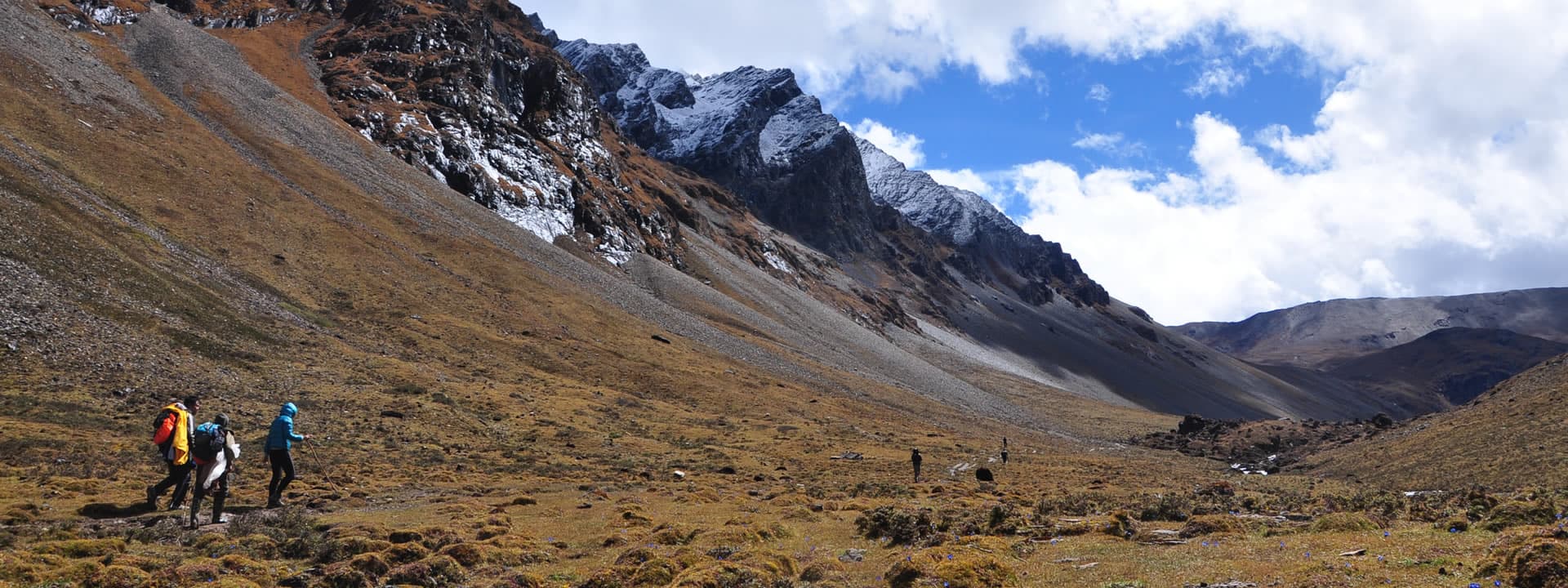 Trekkers walking through a high alpine valley below snow-dusted ridgelines